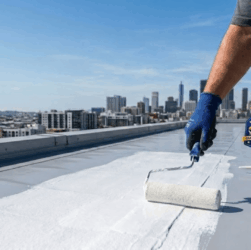 A professional roofer applies a white elastomeric coating to seal a seam on a flat TPO roof to prevent leaks.