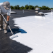 Worker applying white EPDM roof coating with a roller on a flat commercial roof